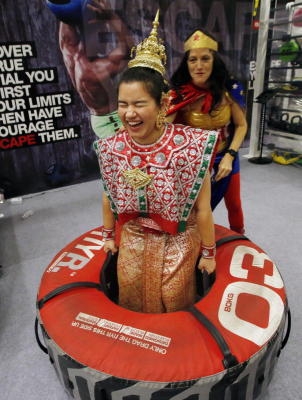 epa04442637 A picture made available 12 October 2014 shows a Thai personal trainer, dressed in a traditional Thai costume is encouraged by another wearing a Wonder Woman costume, as she lifts an 80 kg exercise tire, during the Asia Fitness Convention 2014 held in Bangkok, Thailand, 11 October 2014. The sixth edition of the three-day convention has attracted over 1,300 fitness professionals working in the expanding fitness industry from all over Asia to learn the latest in leading edge fitness education, trends and equipment. EPA/BARBARA WALTON +++(c) dpa - Bildfunk+++