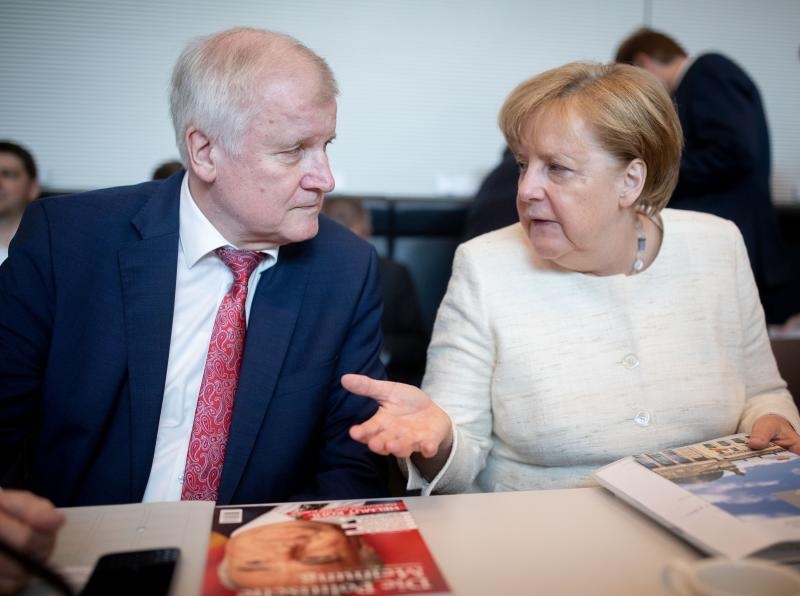 <p>18.06.2018, Bayern, München: Horst Seehofer, CSU-Vorsitzender und Bundesminister für Inneres, Heimat und Bau, läuft auf seinem Weg zu einer Pressekonferenz, die in Anschluss an die Sitzung des CSU-Vorstands stattfindet, an einem Fernseher vorbei, auf dem die Pressekonferenz von Bundeskanzlerin Angela Merkel (CDU) übertragen wird. Foto: Peter Kneffel/dpa +++ dpa-Bildfunk +++</p>